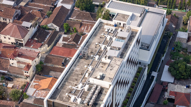 Aerial view of a modern building with HVAC units on its flat roof surrounded by traditional residential houses in Yogyakarta, Special Region of Yogyakarta, Indonesia.