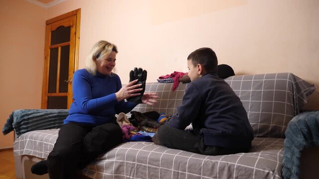Mother and son sort and fold clothes together while talking during a home activity on the sofa.