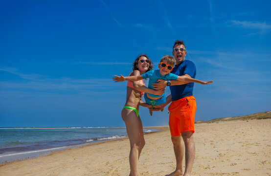 Parents play make fly young son on sunny sandy beach shoreline