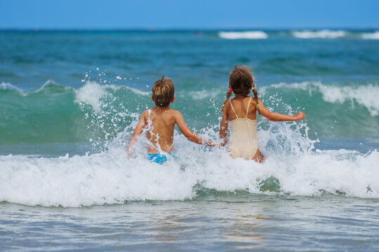 Two children holding hands while playing in ocean foamy waves