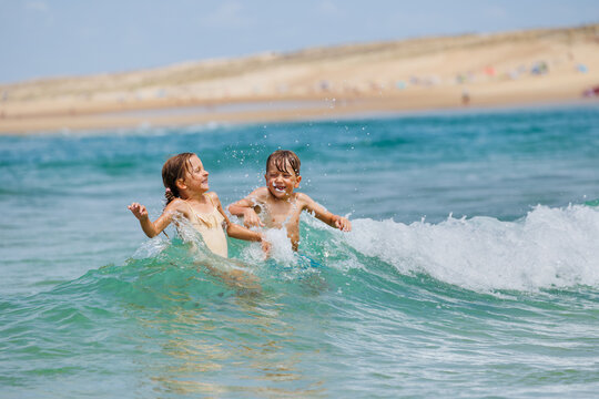 Two children boy and girl splas in ocean waves near sandy beach