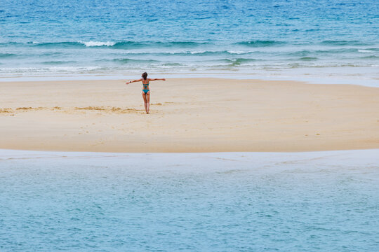 Woman in bikini standing with arms outstretched on sandy beach