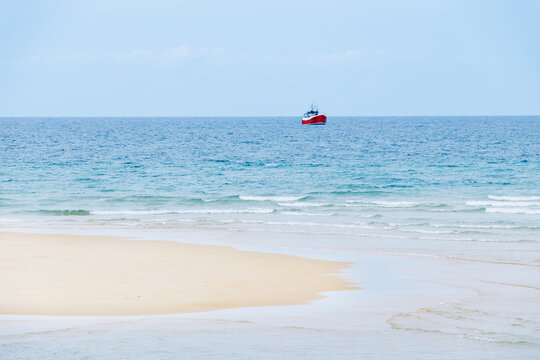 Red fishing boat offshore beyond sandy island under blue sky