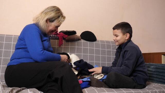 Mother and son sort and fold warm winter clothing, handle garments and work together on household chores.