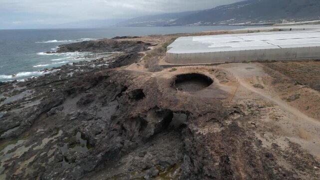 Aerial view of El Rayo sinkhole above rugged sea cliffs near coastal path and plantations