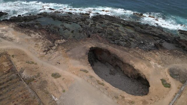 Aerial view of El Rayo sinkhole with fenced edge and lava rocks by Atlantic coast