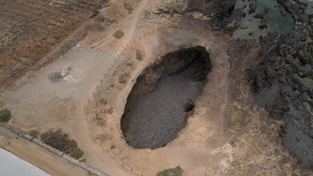 Aerial view circling El Rayo sinkhole and natural arch by rocky Tenerife coastline