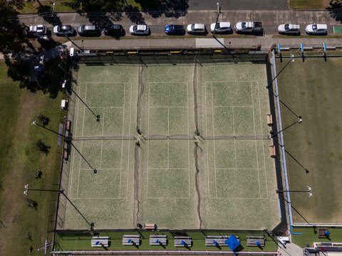 Artificial grass tennis courts from aerial view on sunny day with road visible in background.