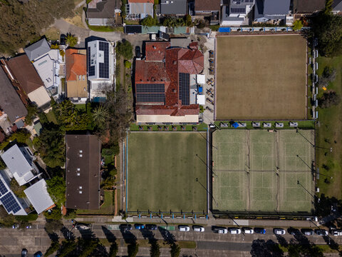 Football field, tennis courts, lawn bowling greens and houses in suburbia from top down aerial view on sunny day. 