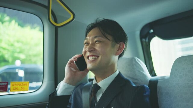 Japanese businessman on the phone in a taxi passing green streets