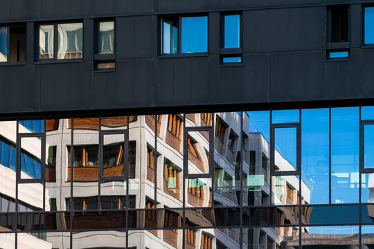 Reflections in modern windows frame surrounding buildings creating a layered urban architectural detail with glass surfaces and city geometry