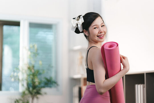 Asian woman holding rolled yoga mat at home for fitness lifestyle