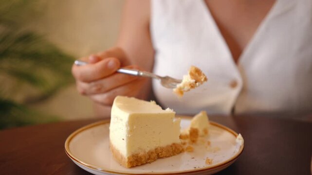 Cheesecake on round plate in cafe. Girl eating cheesecake piece with fork. Horizontal video.