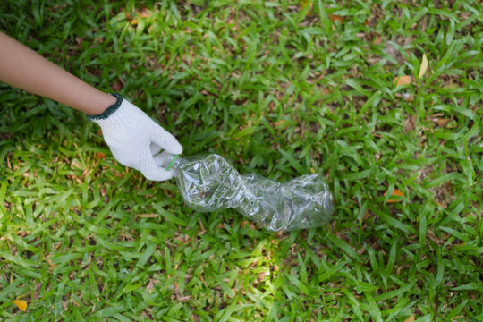 Volunteer hand picking up plastic bottle litter on green grass for environmental cleanup