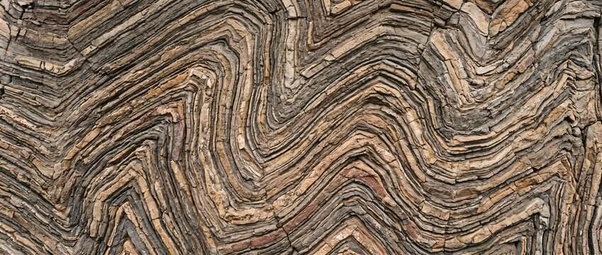 Folded rock strata geological layers texture. Natural sedimentary rock formation with chevron wave folds and compressed stone bedding