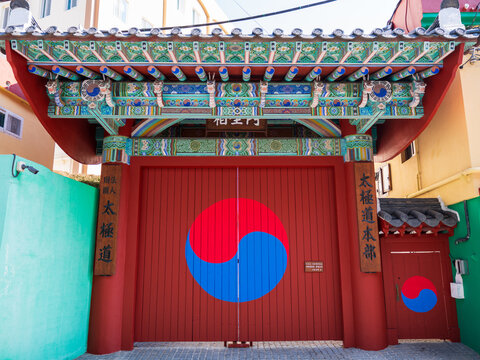 View of the ornate red gate of the Taegeukdo Headquarters featuring a prominent Taegeuk symbol in Gamcheon Culture Village in Busan, South Korea.