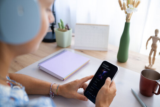 White person holding smartphone listening to music at home office desk