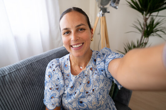 White woman smiling taking selfie indoors on couch with plant and lamp