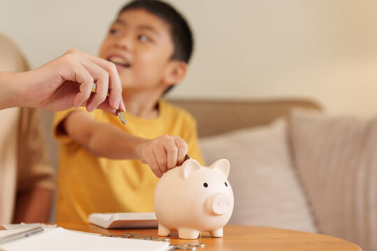 Asian boy putting coin in piggy bank guided by parent for savings habit and education