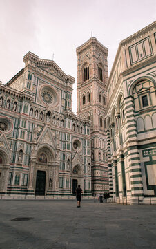 View of the ornate marble facade of the Florence Cathedral and Giotto's Campanile with a person walking in the piazza in Florence, Tuscany, Italy.