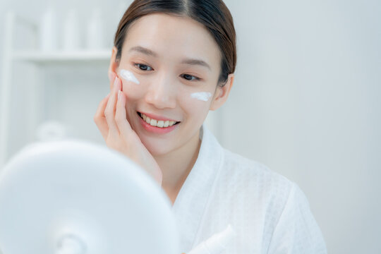 Beautiful Asian woman sit in front of a mirror. face of a healthy woman applying cream and makeup. Advertisement for skin cream, anti-wrinkle, baby face, whitening, moisturizer, tighten pores serum