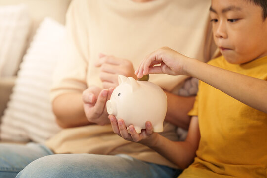 Asian boy putting coin into piggy bank with father at home for financial education