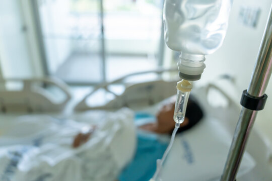 A close-up of a saline bottle strapped to a needle pricked at the hand of a female patient lying in a hospital bed. Medical and treatment of patients concepts