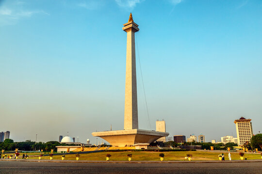 National Monument Monas towering over Jakarta's skyline with mosque dome and city buildings under clear evening sky. Jakarta, Indonesia