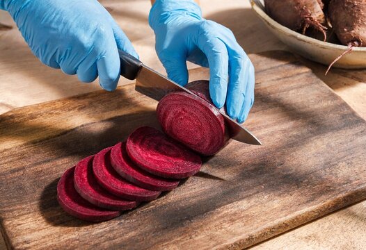 A chef in blue gloves slicing fresh raw beetroot on a rustic wooden cutting board for professional food preparation