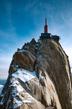 View of the Aiguille du Midi observation deck perched on a jagged, snow-dusted granite peak under a clear blue sky in Chamonix, Auvergne-Rhone-Alpes, France.