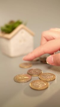 Close-up view of Kazakhstan tenge coins being moved one at a time beside a miniature house, illustrating careful budgeting, saving for housing, financial discipline and long-term financial goals.