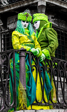 View of two people wearing elaborate green and yellow costumes and masks standing on a balcony during the Venice Carnival in Venice, Veneto, Italy.