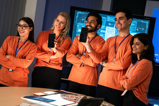 A group of tech professionals stand together in an office holding up smartphones to display new mobile apps, sharing a moment of excitement and pride in their project development work.