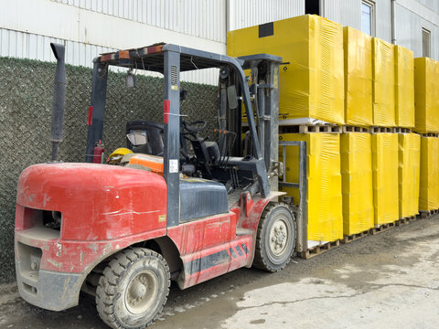 View of a red forklift transporting a stack of yellow-wrapped pallets in an industrial area in Istanbul, Istanbul, Turkiye.