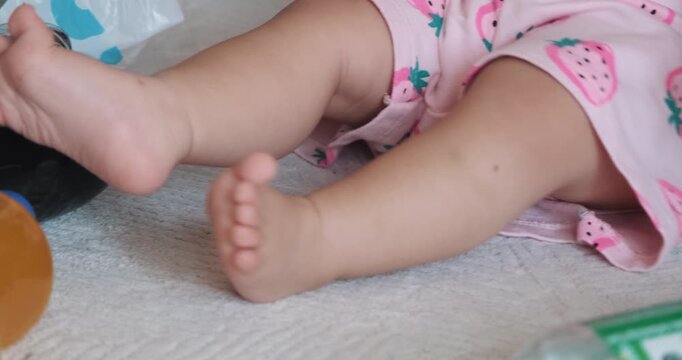 Close up of baby girl in pink strawberry romper kicking and playing with plastic beverage bottle on floor
