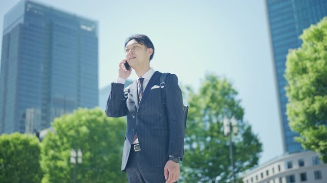 Japanese businessman on a phone call below glass office towers