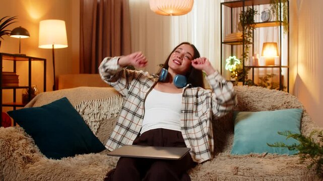 Young woman on home sofa closes laptop after work stretches with relief and smiles at home. Adult girl on home sofa ends online work exhales with ease and enjoys calm rest after home office routine.