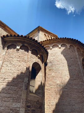 Low-angle view of the curved stone apses of a Romanesque church under a blue sky