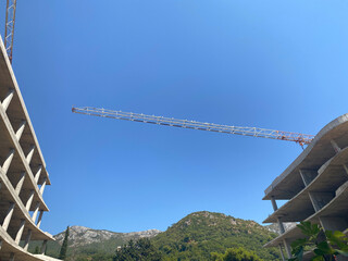 Construction crane boom stretches across a clear blue sky between two unfinished concrete building structures © lmot11