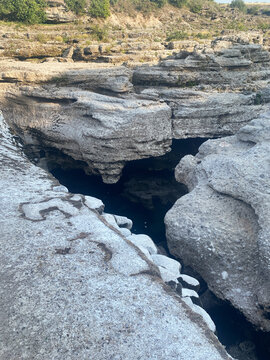 High-angle view of a deep rocky ravine with dark water pooled in a narrow crevice between layered limestone formations