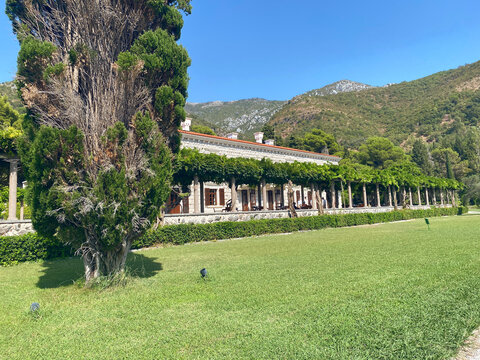 Historic stone villa with a long vine-covered pergola stands next to a manicured lawn