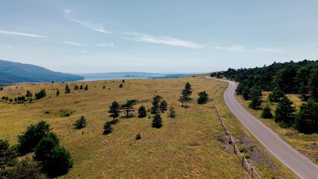 Aerial video overlooking a rugged coastal landscape where forested hills and golden mountain meadows descend toward the deep blue Adriatic Sea