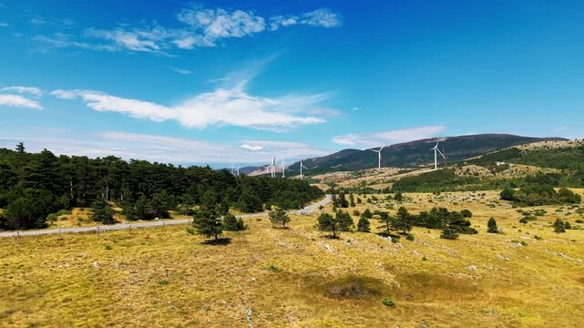 Video showing a mountain plateau covered with grass, scattered rocks and low vegetation, with multiple wind turbines standing along the ridges