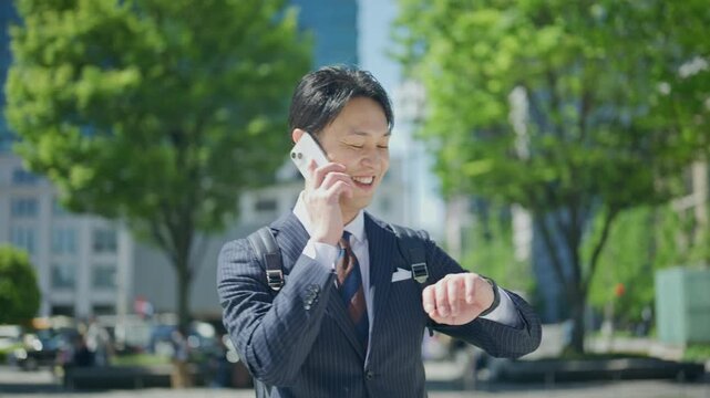 Businessman looking at his watch while talking on the phone in the city