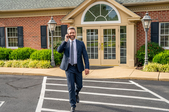 American businessman has phone call. Real estate agent at house for sale. Realtor walking and talking on phone. Rent or buy new home. Home insure. Property insurance promotion. Successful broker