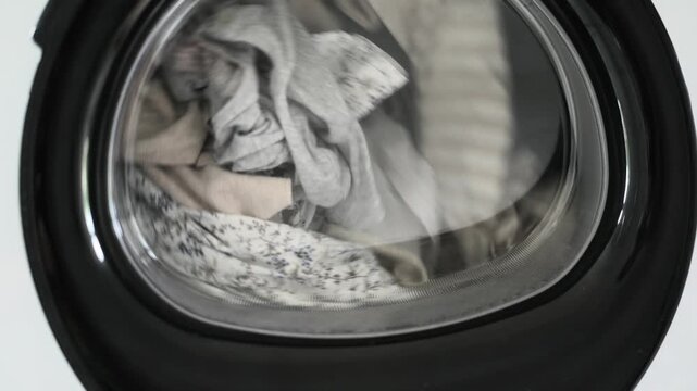 Light colored clothes vigorously spin inside front load washing machine drum.