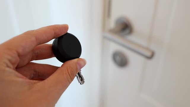 Hand holding an RFID key fob in front of an apartment door with lock and handle. Concept of electronic access control, keyless entry and residential security.