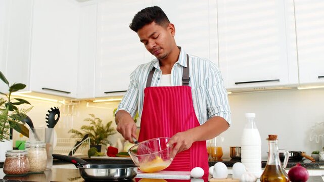 Indian man whisking eggs in glass bowl for omelet during focused breakfast prep in home kitchen. Arabian guy making simple protein meal for diet routine and clean eating before office work with focus.