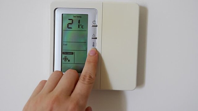 Hand adjusting a digital thermostat set to 22 degrees on a modern wall mounted climate controller. Smart home technology, indoor comfort and energy efficient temperature control.