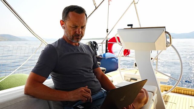 Focused man working on laptop aboard a sailing yacht. Productive remote office in a unique travel environment.